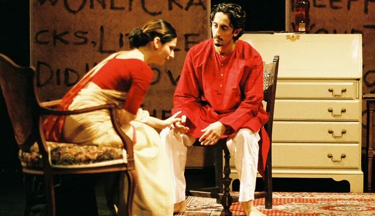 Two actors mid-scene in a Shunya production, in red against a hand-lettered set